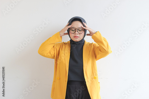 beautiful young Asian Muslim woman, wearing glasses and yellow blazer with dizzy expression holding head © Muchlis Nugroho