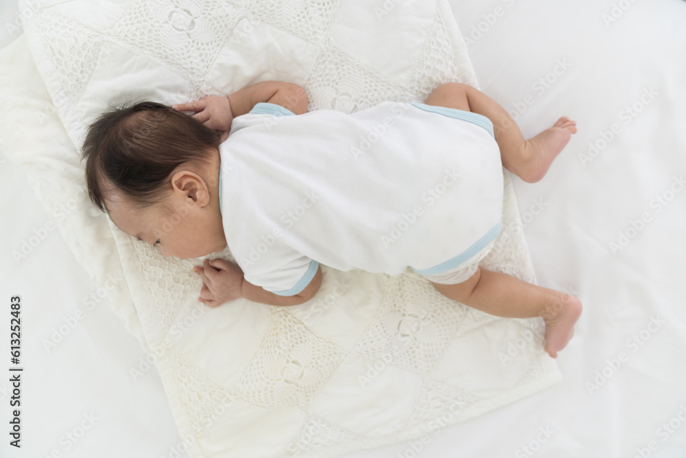 Top view of newborn baby sleeping on blanket on white bed. Infant lying
