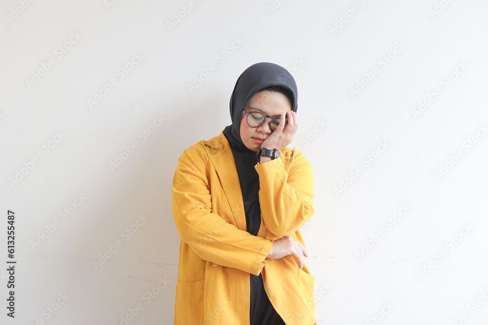 Beautiful young Asian Muslim woman, wearing glasses and yellow blazer covering 1 side of face with hand Beautiful young Asian Muslim woman, wearing glasses and yellow blazer covering 1 side of face with hand