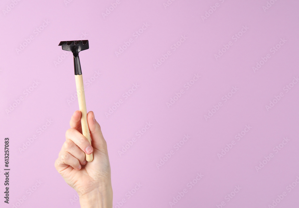 Hand holding mini gardening tool (rake) on purple background Hand holding mini gardening tool (rake) on purple background