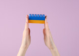 Female hands hold yellow and blue blocks of children's plastic constructor in the colors of the Ukrainian flag on a purple background