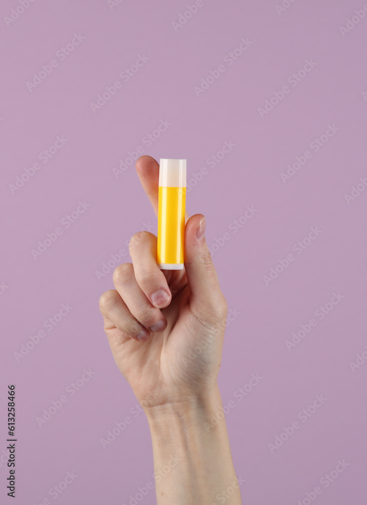Woman's hand holds tube of lip balm on pastel background Woman's hand holds tube of lip balm on pastel background