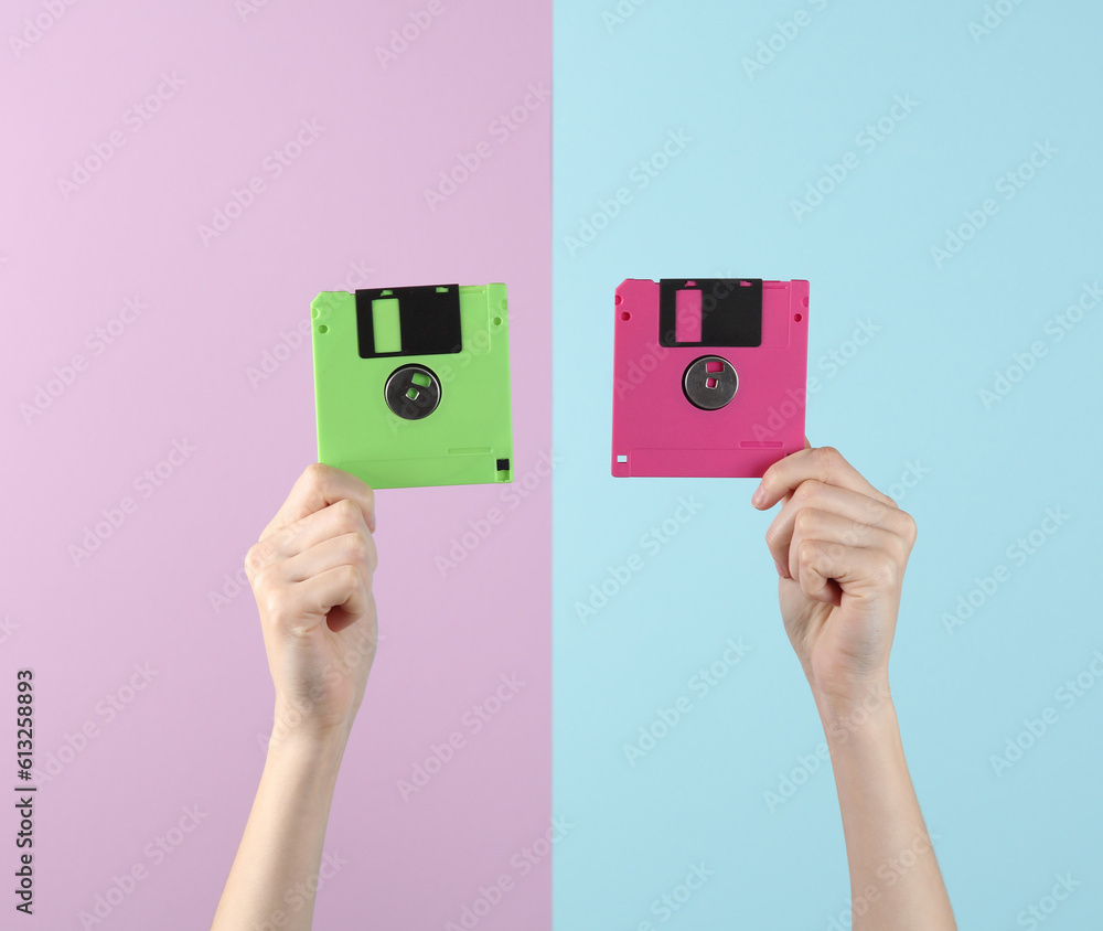 Female hands hold two colored obsolete floppy disks on a blue-pink pastel background. Retro 80s Female hands hold two colored obsolete floppy disks on a blue-pink pastel background. Retro 80s