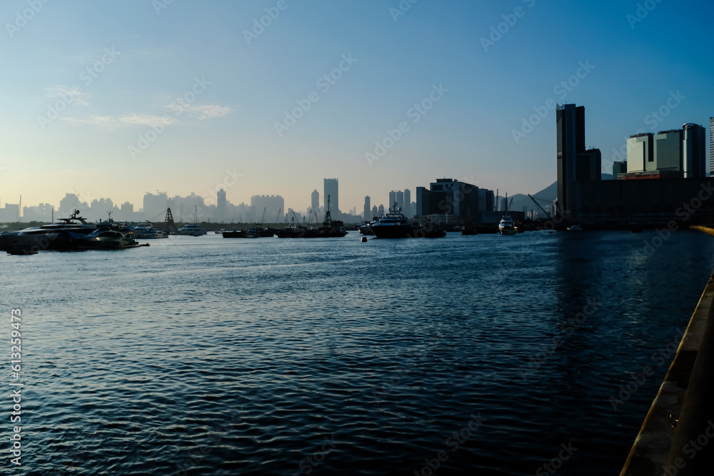 The calm seascape with skyscrapers, urban skyline in the background under the sunset. Hong Kong city view with boats on the sea. Travel scene, city scene and cityscape.