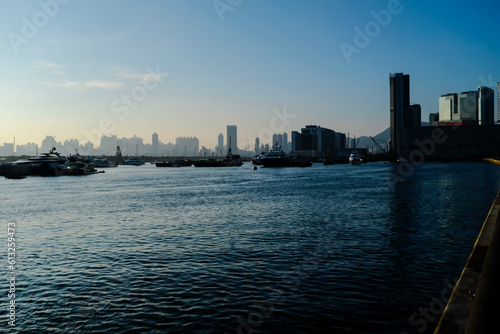 Fototapeta Naklejka Na Ścianę i Meble -  The calm seascape with skyscrapers, urban skyline in the background under the sunset. Hong Kong city view with boats on the sea. Travel scene, city scene and cityscape.