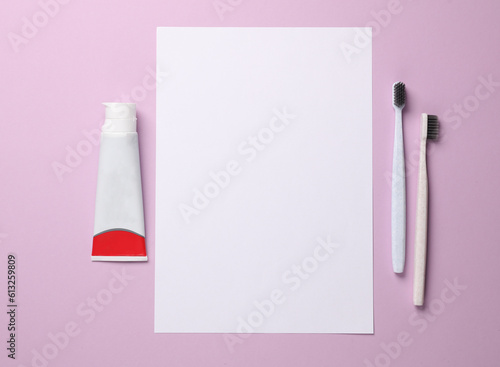 Two toothbrushes and tube of toothpaste, paper sheet on a purple pastel background. Copy space. Top view