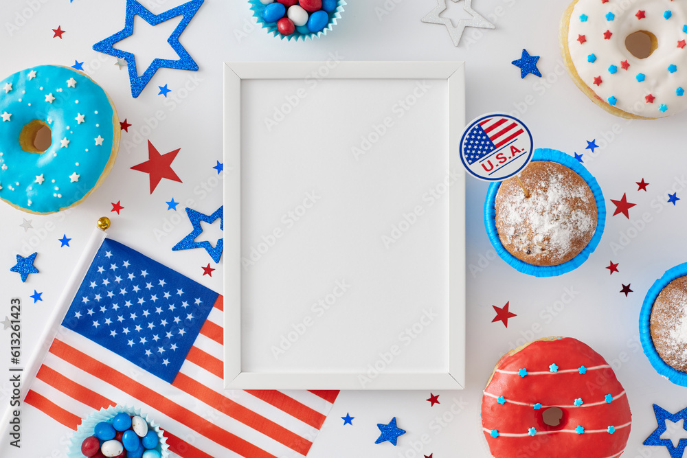Obraz premium Fourth of July celebration theme for a party. Top view arrangement of donuts, cupcakes, american flag and stars on white background with blank frame for text or advert