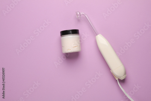 Acne treatment. Device for local darsonvalization with cream jar on a purple background. Beauty concept. Flat lay. photo