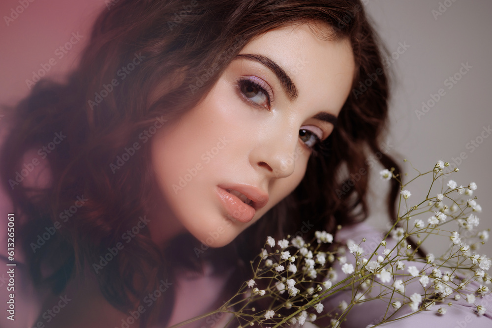 A beautiful brunette girl with natural make-up looks at the camera holding a bouquet of white gypsophila flowers in her hands. The concept of congratulations on March 8, valentine's day.