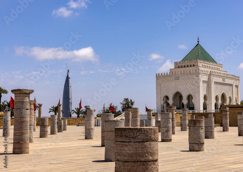 Remains of the unfinished Great Mosque in Rabat, Moroccan flags waving and the Mohammed VI Tower in the background.