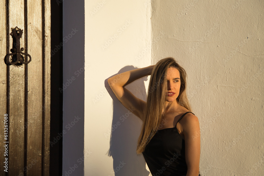 Fototapeta premium Young woman, beautiful and blonde, with black tank top receiving the last rays of afternoon sun with sensual and provocative attitude. Concept sensuality, provocation, flirting, beauty.