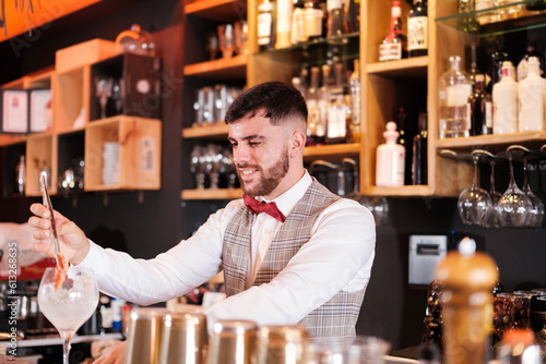 Young bartender creating a cocktail with a red bow tie. Concept: drinks, nightlife, lifestyle