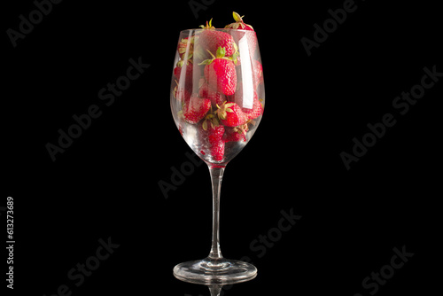 Several red strawberries in a glass goblet, macro, isolated on black background.