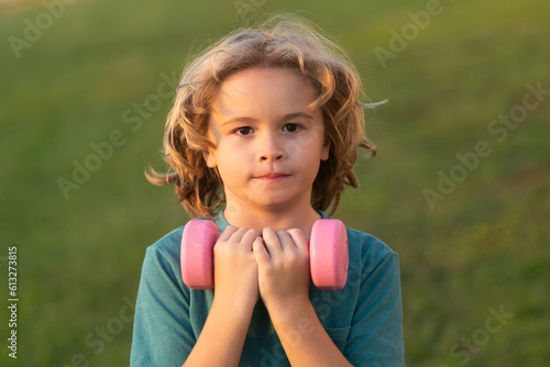 Cute little boy doing exercises with dumbbells. Portrait of sporty child with dumbbells. Happy child boy exercising. Healthy activities kids lifestyle.