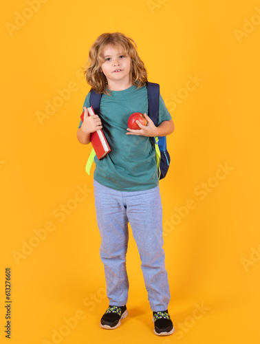 Kid from school. School child in school uniform with bagpack book and apple. School children on studio isolated yellow background.