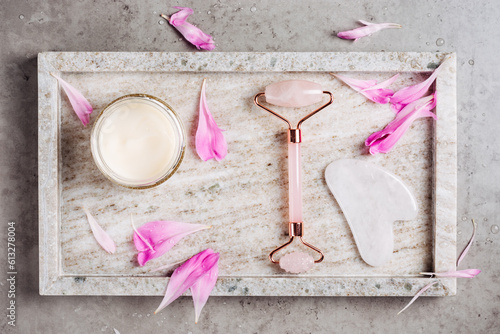 Rose quartz roller and gua sha on a marble background with flower petals.