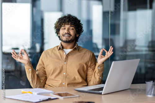 Fotomurale Successful hispanic man resting in office relaxing, businessman meditating in lotus position at workplace, with laptop doing yoga during break