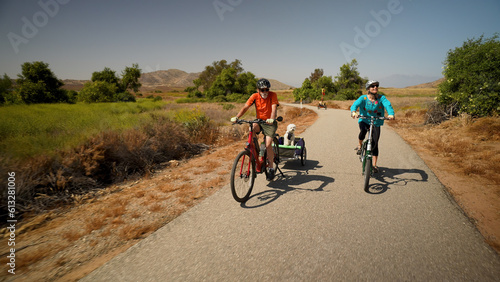 Elderly senior man biking on an electric bike on a trail pulling a trailer with a dog in it with a mature woman on an e-bike next to him. © Robert Peak