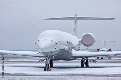 Private white business jet jet stands at the airport under the snow in winter against a cloudy sky close-up