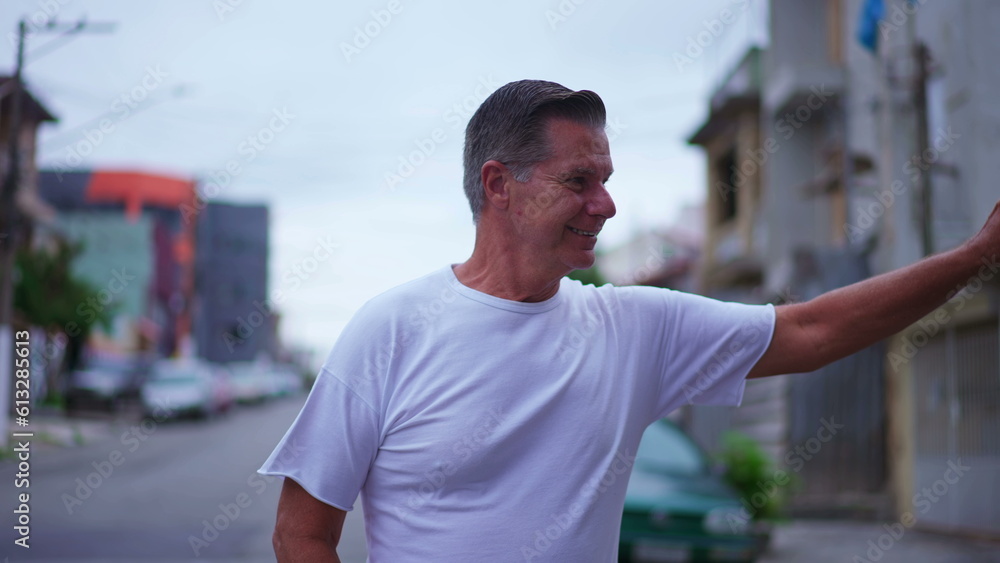 Happy older man waving hello to neighbors while walking in street. A middle-age caucasian male person walks forward toward camera while greeting to friends around him