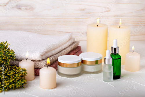 Cosmetics, burning candles, towels and juniper branch on light background. Cream or lotion, oil or gel, skin care, spa treatments. Selective focus