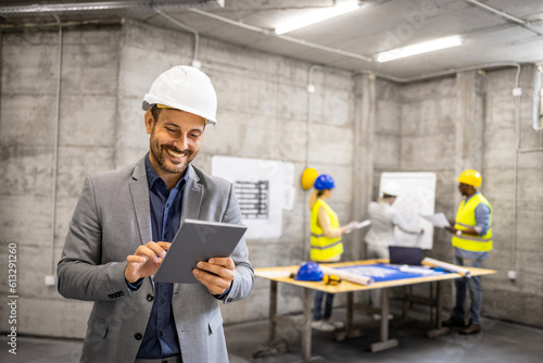 Portrait of structural engineer in business suit and hardhat working on tablet computer at construction site.