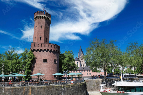 Cologne (Köln, Rheinauhafen, Malakoffturm), Germany - June 6. 2023: Beautiful rhine riverside beer garden restaurant terrace at medieval fortress with stone tower photo