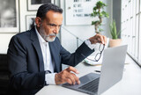 Focused sad confident european old businessman in suit looks at laptop, create idea in office