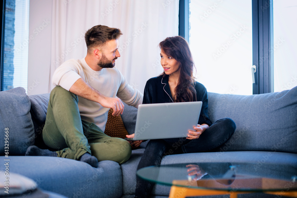 Smiling woman and man sitting together at home and using laptop Smiling woman and man sitting together at home and using laptop