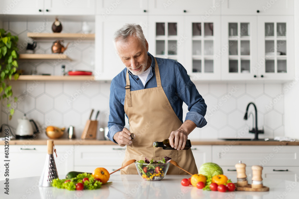 Smiling senior man cooking fresh vegetable salad in kitchen Smiling senior man cooking fresh vegetable salad in kitchen