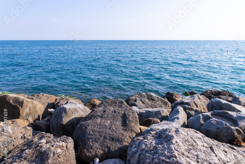 Tranquility rocky beach with big black stones, blue sea and sky as background, tranquil and looks beautiful.Big stone beach in front of sea with sky
