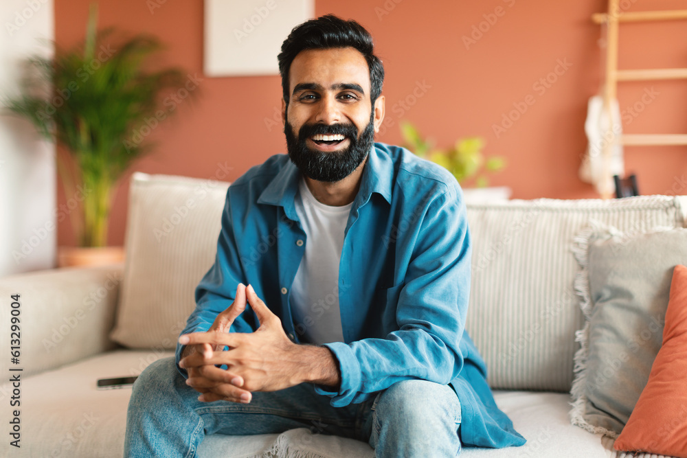 Happy indian man relaxing sitting on couch at modern home