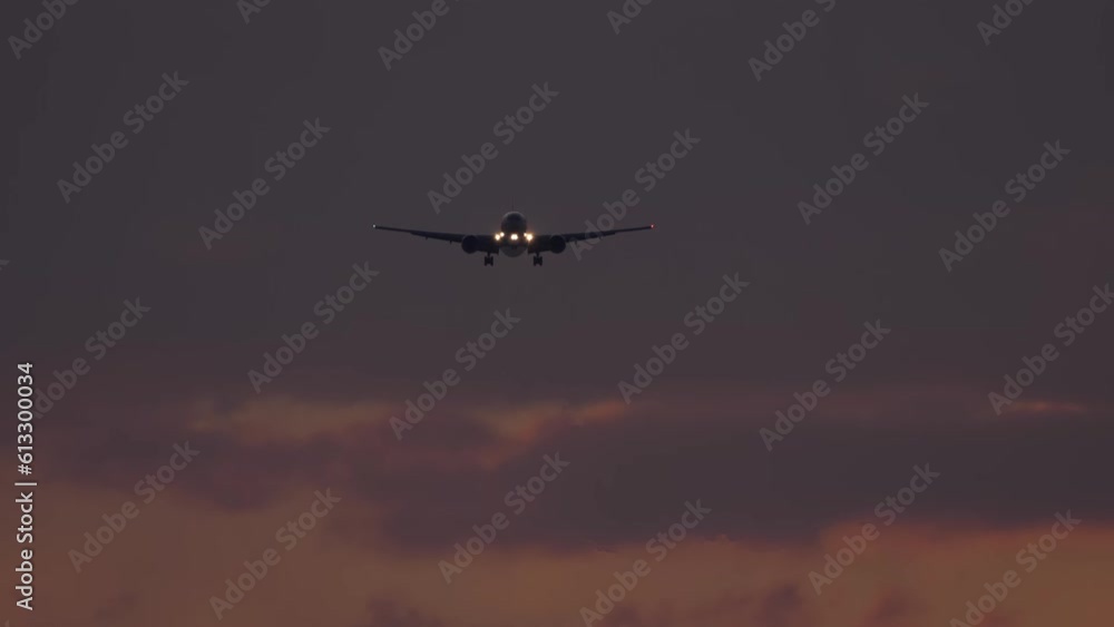 Jet plane approaching to land, silhouette in the night. Airplane flies with headlights on. Airliner flies at dusk