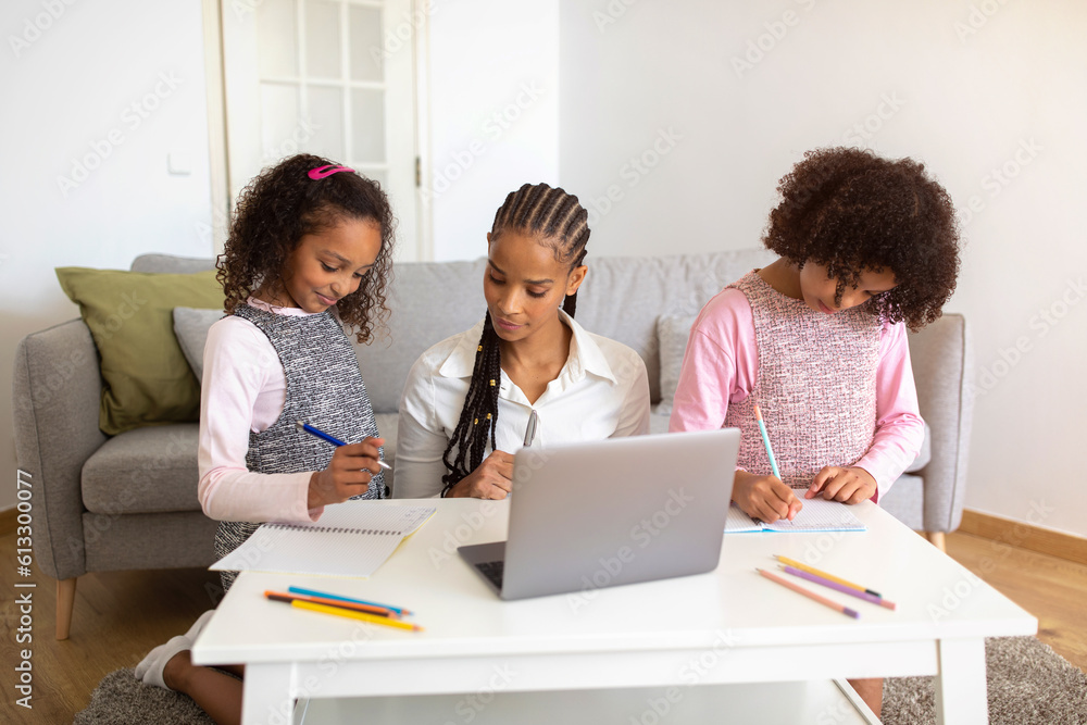 Black mother at laptop helping her daughters with homework indoor Black mother at laptop helping her daughters with homework indoor