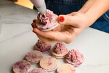 Close up horizontal shot of chef woman squeezing pink fruit ganache cream on macarons halves