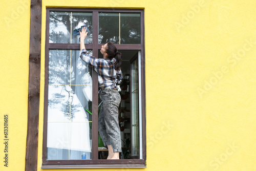 A woman manually washes the window of the house with a rag with a spray cleaner and a mop outside. Safety at height, restoring order and cleanliness in the spring, cleaning service © Ольга Симонова