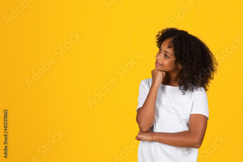 Happy pensive curly teenager black schoolgirl in white t-shirt thinks, chooses, looks at empty space