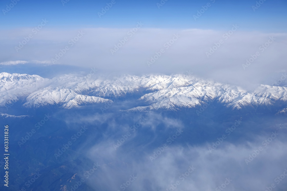 View of the high snow-capped peaks of the Main Caucasian Range from the window of a flying aircraft View of the high snow-capped peaks of the Main Caucasian Range from the window of a flying aircraft