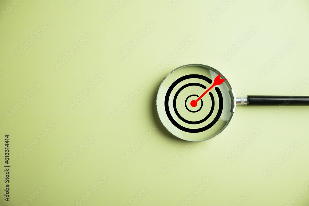 A magnifier glass focuses on a target board, symbolizing the business objective, target search concept, and achieving success. Isolated on a background with copy space. A magnifier glass focuses on a target board, symbolizing the business objective, target search concept, and achieving success. Isolated on a background with copy space.