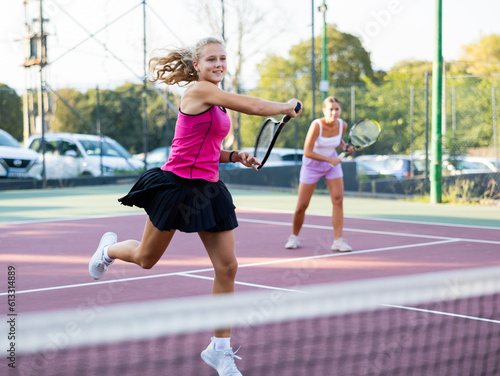 Young woman in sport skirt playing tennis on court. Racket sport training outdoors