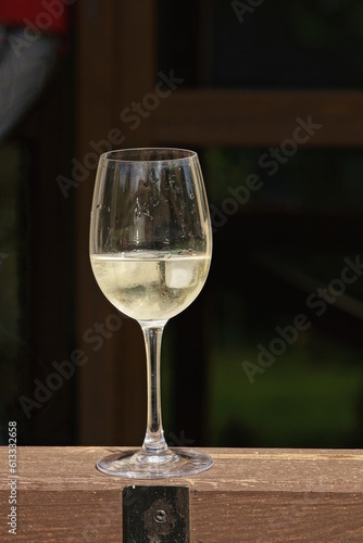 one white glass goblet with yellow wine and pieces of ice stands on a brown wooden table outdoors on a gray background