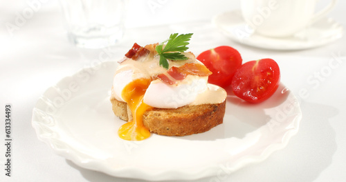 toast with poached egg and bacon on a plate. serving breakfast on a white plate with tomato. sunny day. angle view. 
