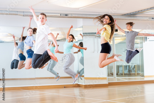 Group of cheerful teenagers dancing and jumping in dance studio during class, side view