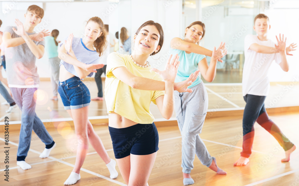 Portrait of cheerful teenage girl doing exercises during group class in dance center