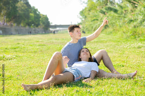 Young girl is resting on her boyfriend's lap, who's sitting on the grass