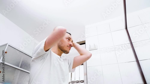 Light-skinned Hispanic Latino man combs his hair with water in front of the bathroom mirror at home