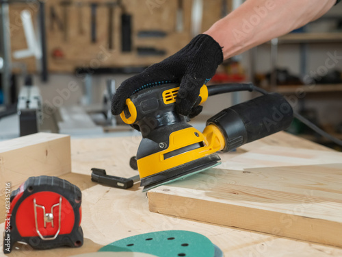 A man using an orbital wood sander in a workshop. Close-up of a carpenter's hands. photo