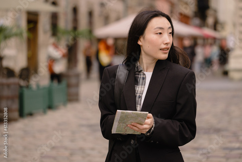 Portrait young happy asian woman tourist in casual clothes on old city street in europe while checking direction on map and navigation on smartphone