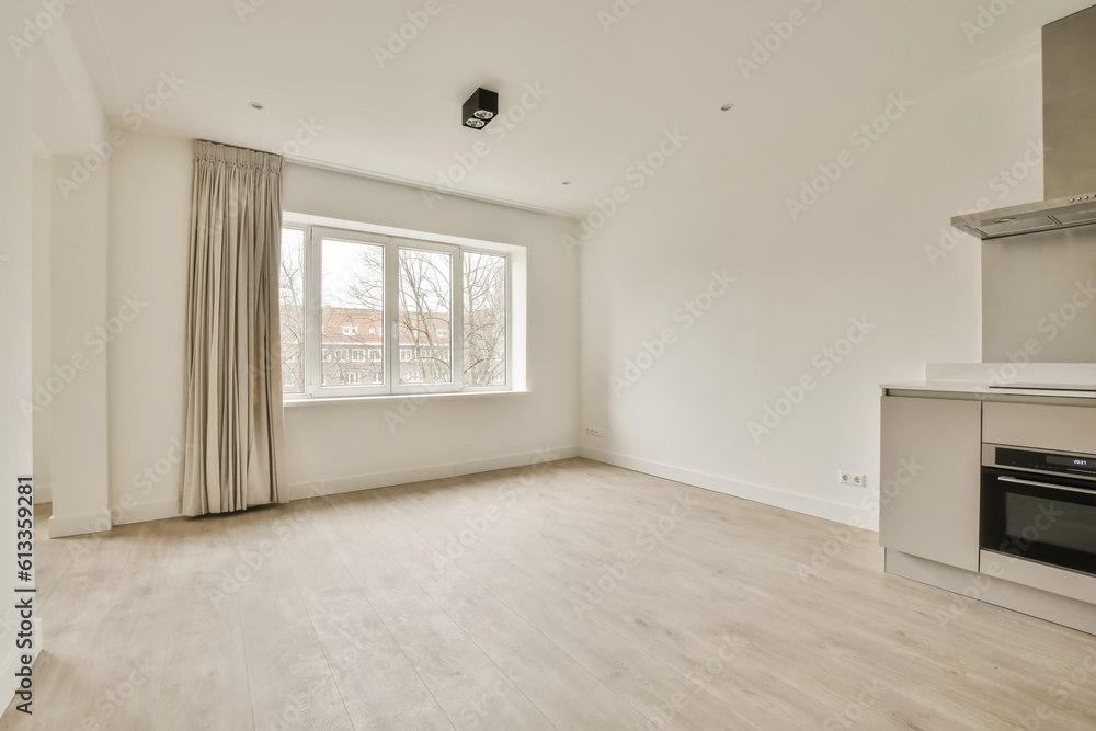 an empty living room with white walls and hardwood flooring in a kitchen area is visible on the right side an empty living room with white walls and hardwood flooring in a kitchen area is visible on the right side