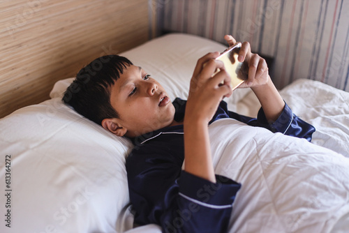 Addicted little boy wearing pajamas under the blanket playing games on phone in bed time. Social media and games online addicted concept and lifestyle